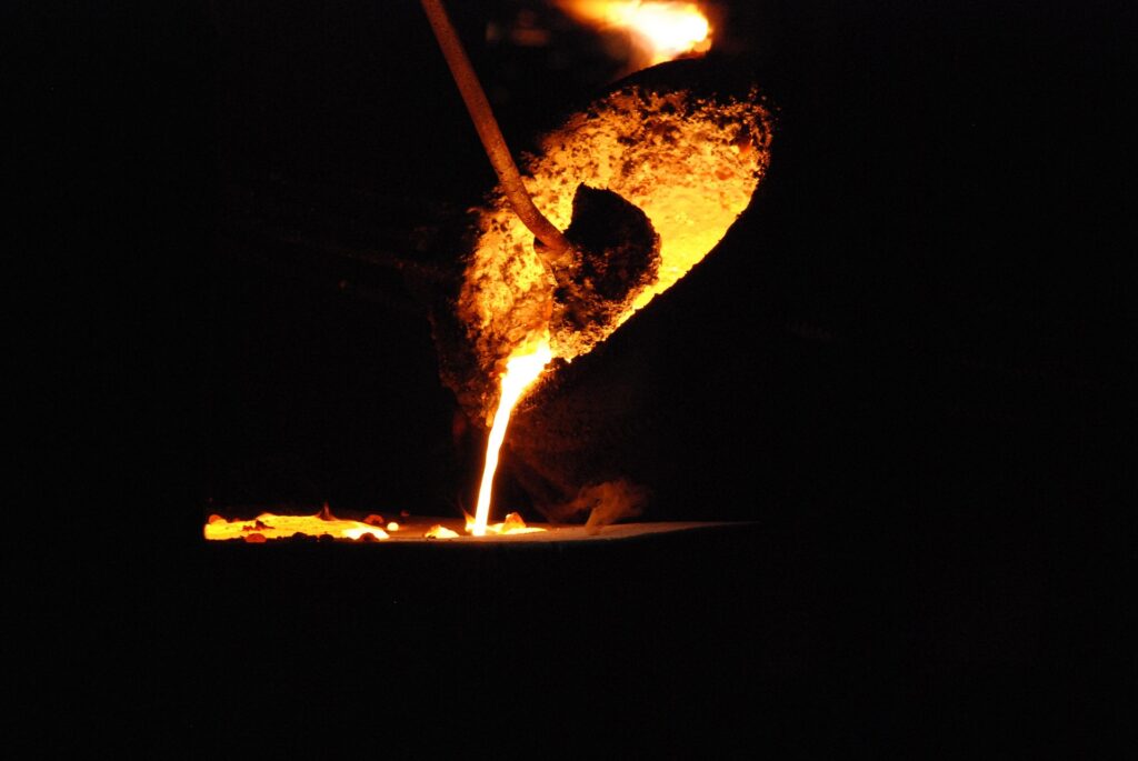 A molten metal pour from a crucible, glowing in the dark, showcasing the intense heat and craftsmanship of metalworking.