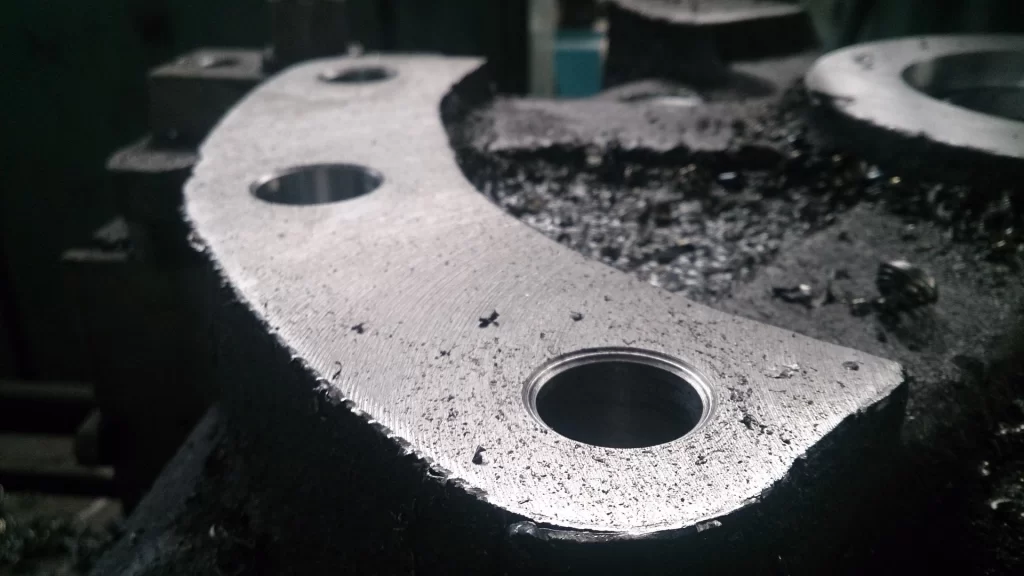 Close-up of a metallic surface with drilled holes and metal shavings, highlighting high precision machining services.
