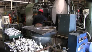 Worker in a factory setting operating machinery, surrounded by piles of molded items and industrial equipment.