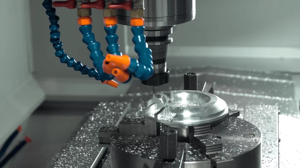 Close-up of a CNC milling machine cutting a metal part, with coolant hoses feeding fluid to the tool and metal shavings scattered around.