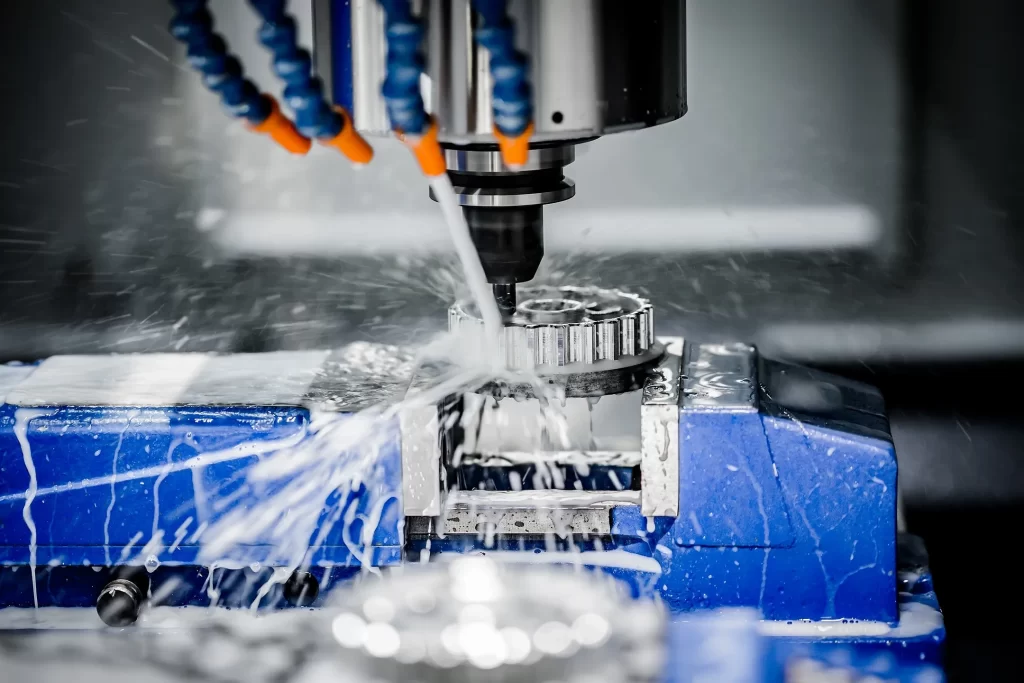 Close-up of a CNC machine tool cutting metal, with coolant spraying and metal shavings being produced on a blue work surface.