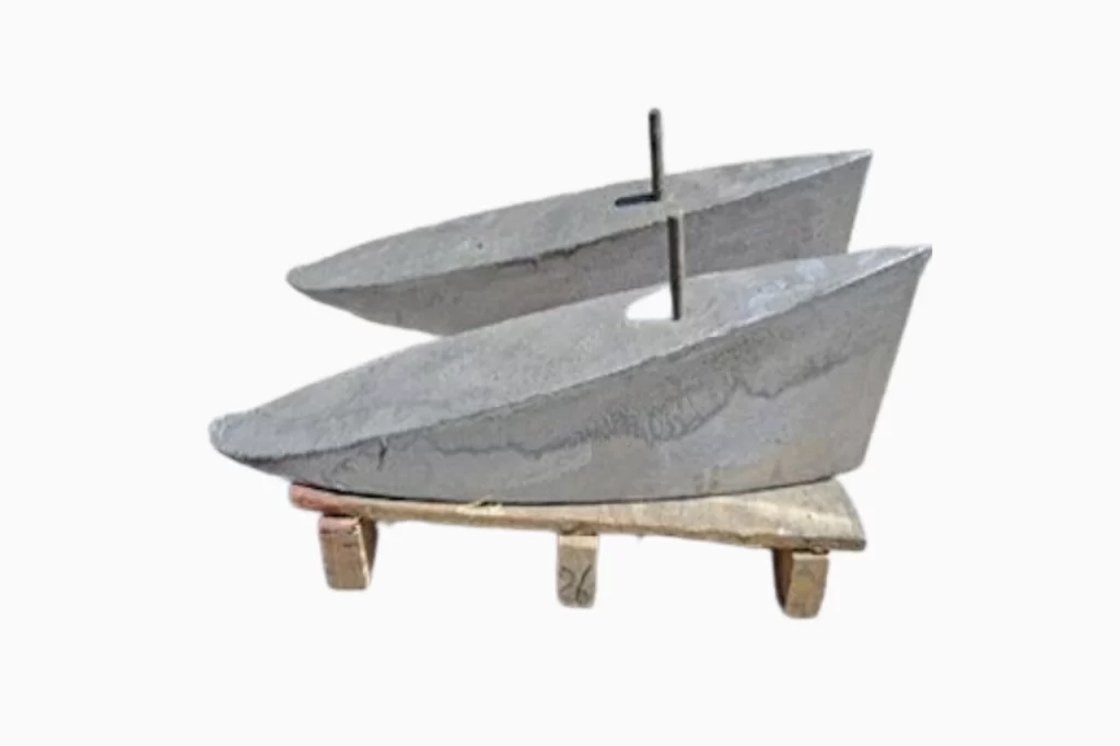 Abstract sculpture of two boat-shaped forms made of concrete, mounted on a wooden base with a vertical metal pole.