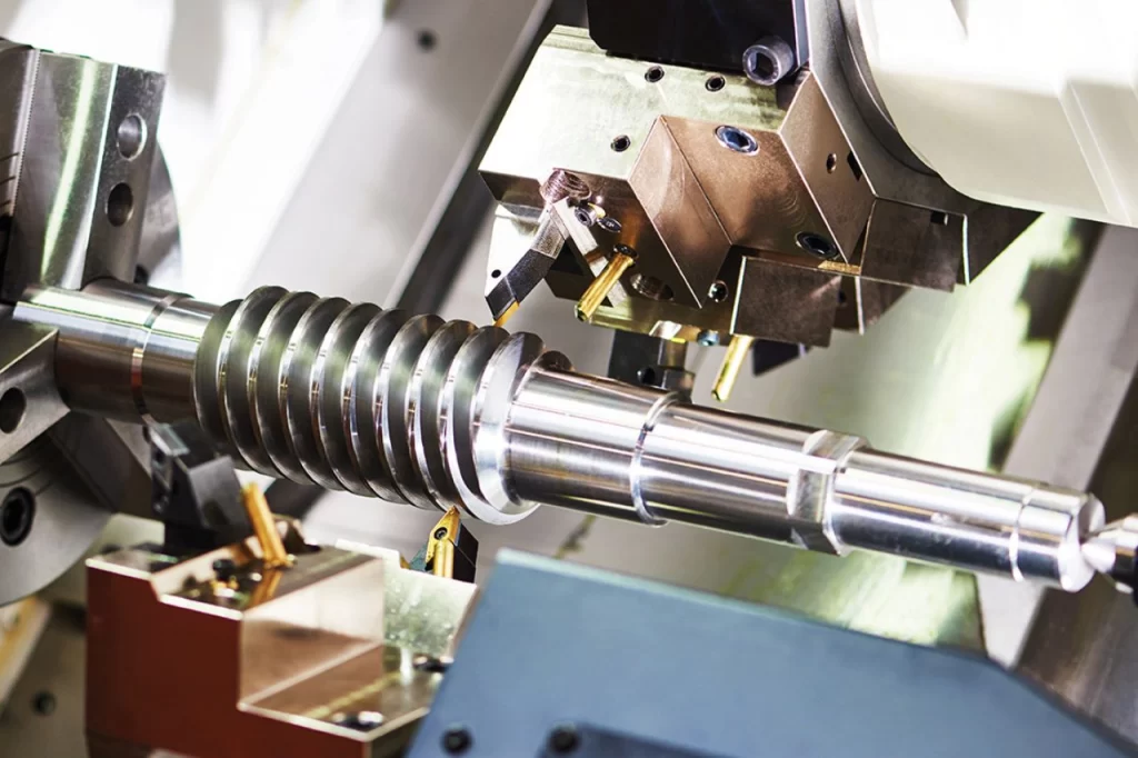 Close-up of lathe works on a precision-engineered metallic component being machined, showcasing intricate grooves and tools in a manufacturing setup.