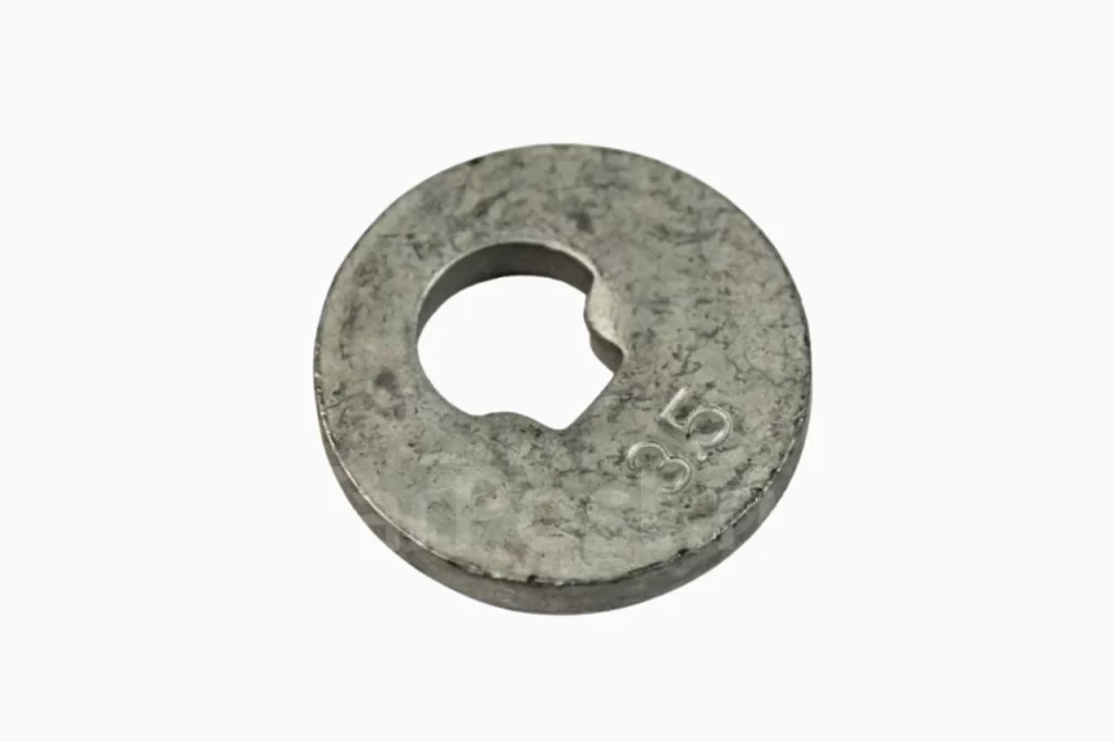 Close-up of a metallic washer with a central hole and a slight irregular shape, showing signs of wear and a stamped number.