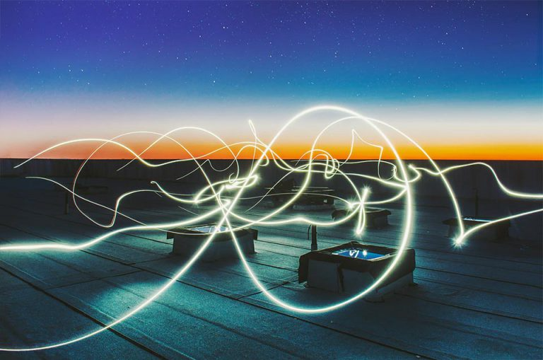 A rooftop at dusk with swirling light trails against a gradient sky of deep blue and orange, dotted with stars.