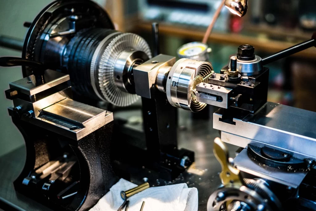 Close-up of lathe works on a precision lathe machine in a workshop, with a metal part being machined under bright lighting.