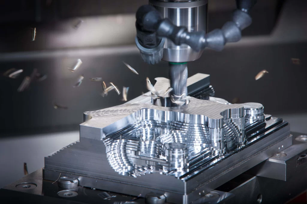 A close-up of a CNC milling machine cutting intricate patterns into a metallic workpiece, with metal shavings flying off.