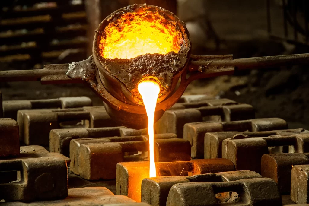 Molten metal pours from a crucible into molds during an aluminum bronze casting process, glowing orange against a dark industrial backdrop, showcasing a metalworking process.
