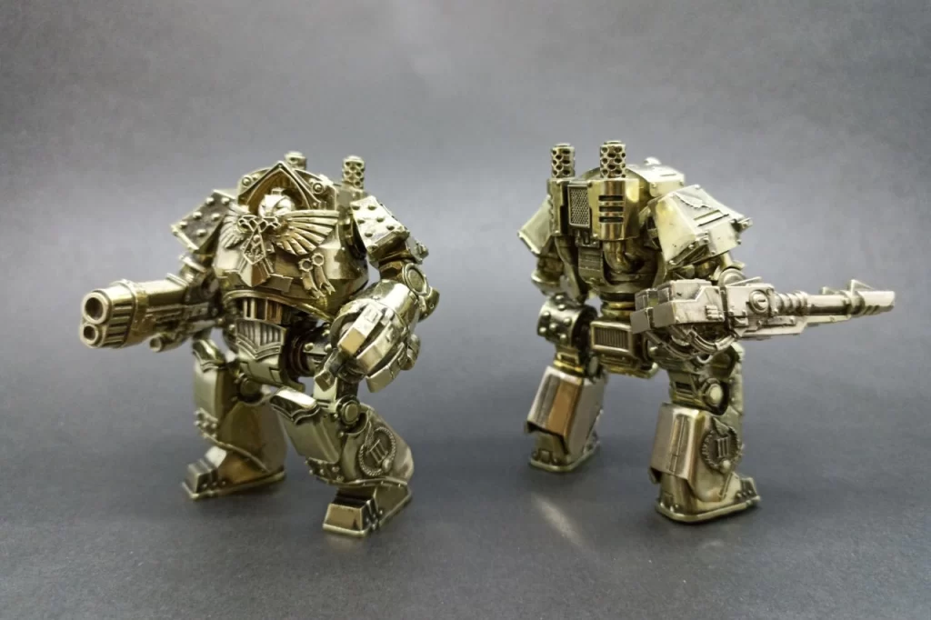 Two detailed metallic robots, one with a large cannon and the other with a rifle, posed against a dark background.