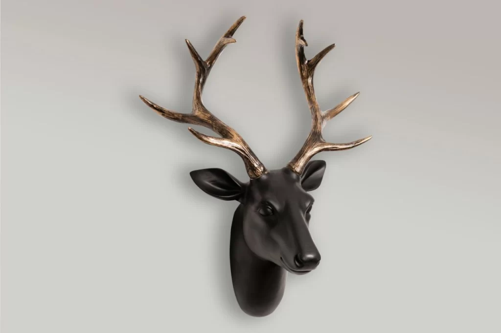 A black deer head wall mount with gold-tipped antlers against a light gray background, showcasing modern decor style.