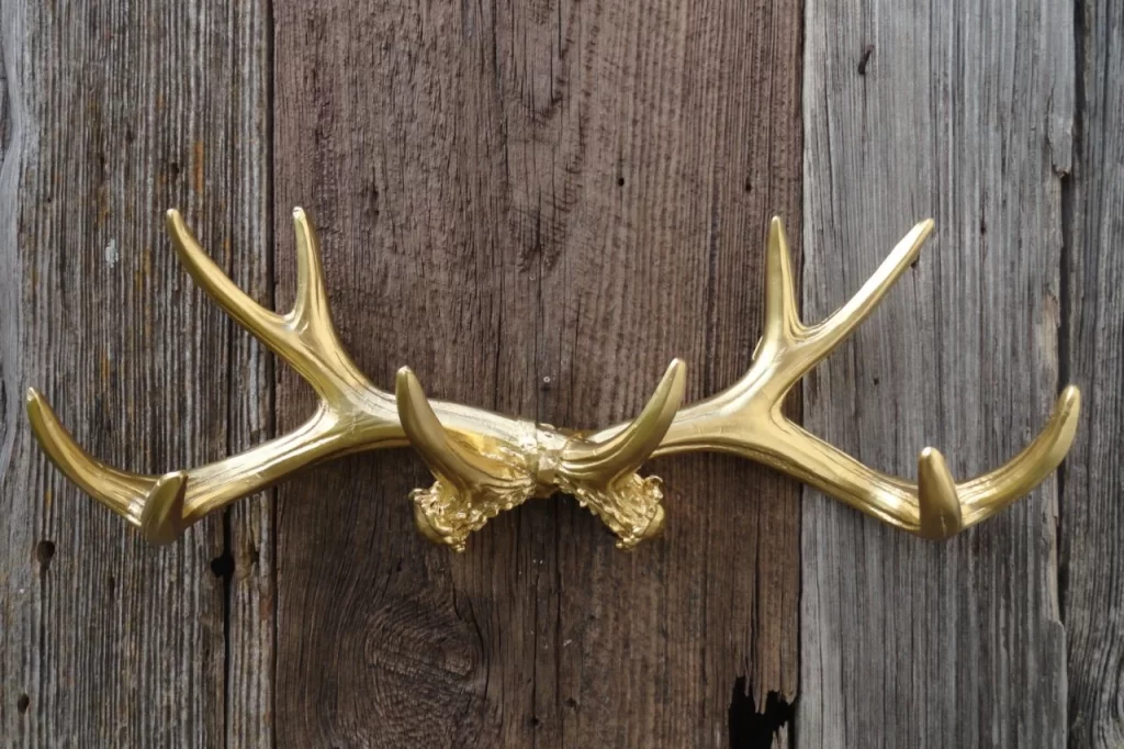 Gold decorative deer antlers mounted on a rustic wooden background.