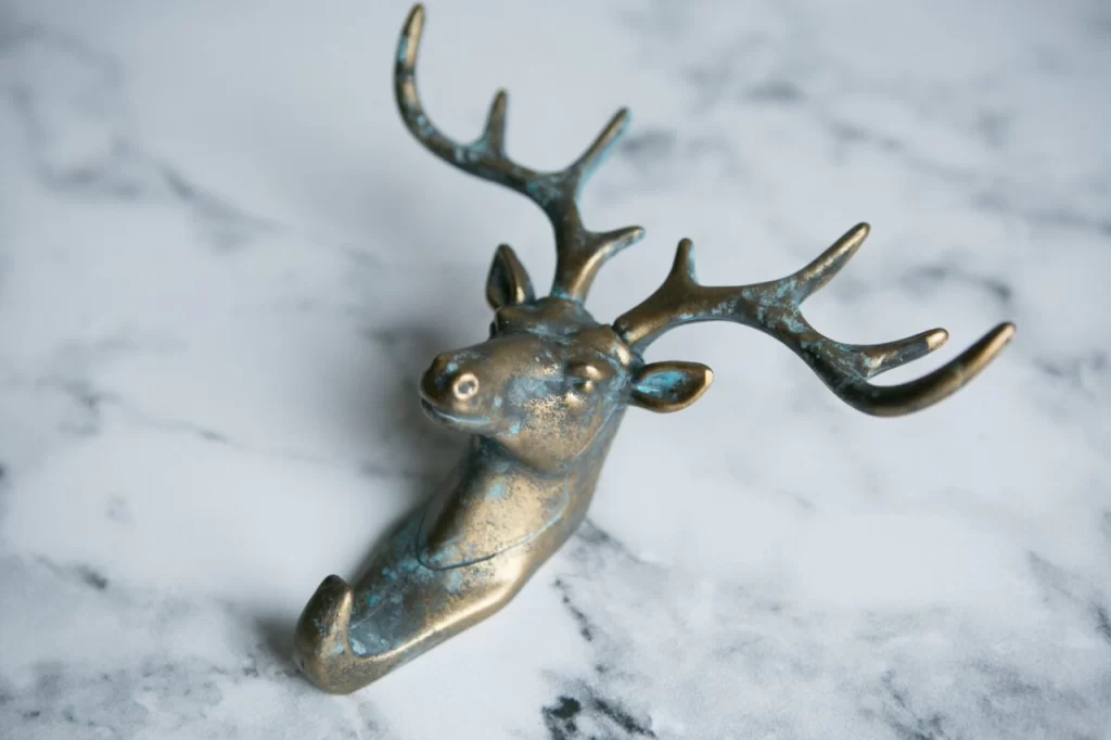 A stylish, bronze deer head hook with antlers, resting on a marble surface, blending functionality with rustic decor.