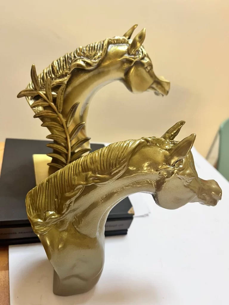 "Two gold horse head sculptures on a table, highlighting their artistic design, luxurious finish, and expert craftsmanship by a metal casting company.