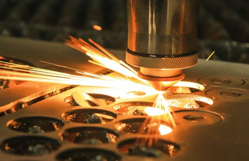 A close-up of a laser cutting machine in action, emitting sparks as it precision-cuts metal plates in intricate shapes.