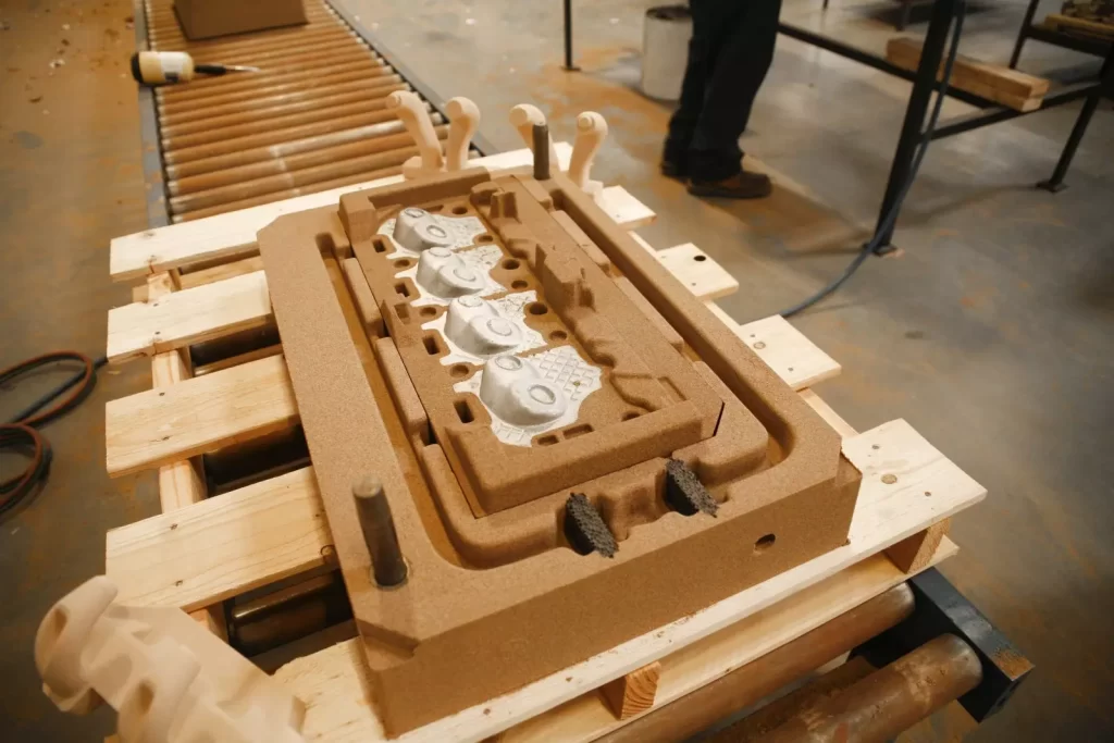 A wooden mold with indentations sits on a wooden pallet, surrounded by tools in a workshop, indicating a manufacturing process.