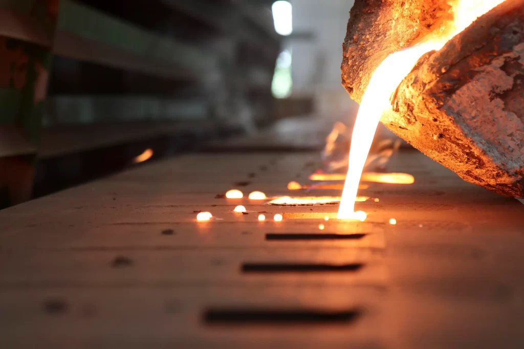 Close-up of a worker shaping a freshly cast aluminum component using precision tools.
