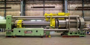 Industrial hydraulic machine used in machining services, featuring a green and yellow frame with cylindrical parts, placed on wooden pallets in a factory.