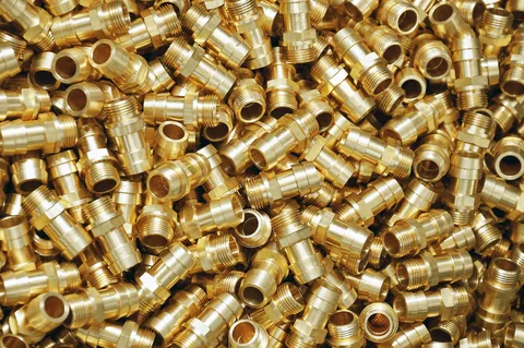 A close-up view of numerous shiny brass fittings and connectors from brass casting, arranged haphazardly to showcase their intricate designs and high-quality craftsmanship.