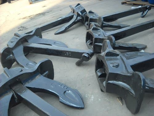 A collection of large black anchors laid out on a concrete surface, designed with sturdy construction and built for saltwater corrosion resistance.