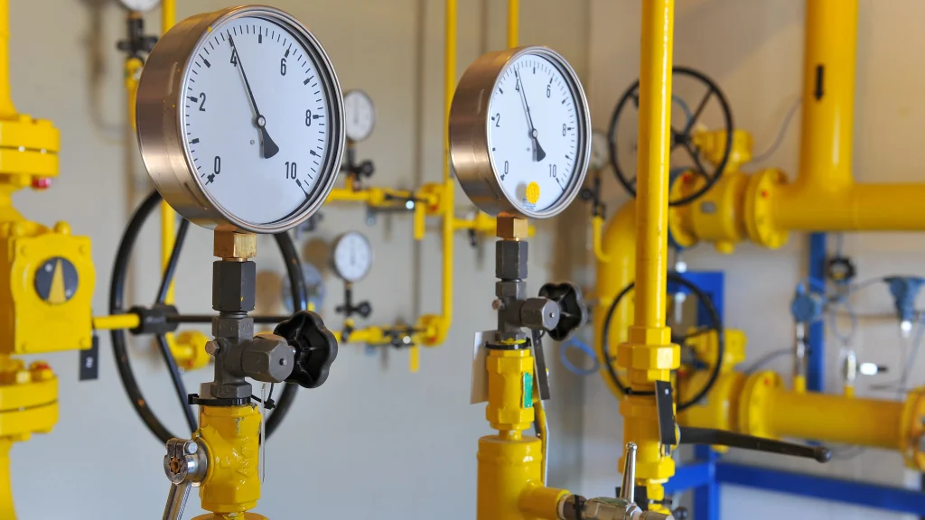 Two pressure gauges on yellow piping and valves in an industrial setting, used for hydraulic pressure testing awareness in gas or fluid systems.