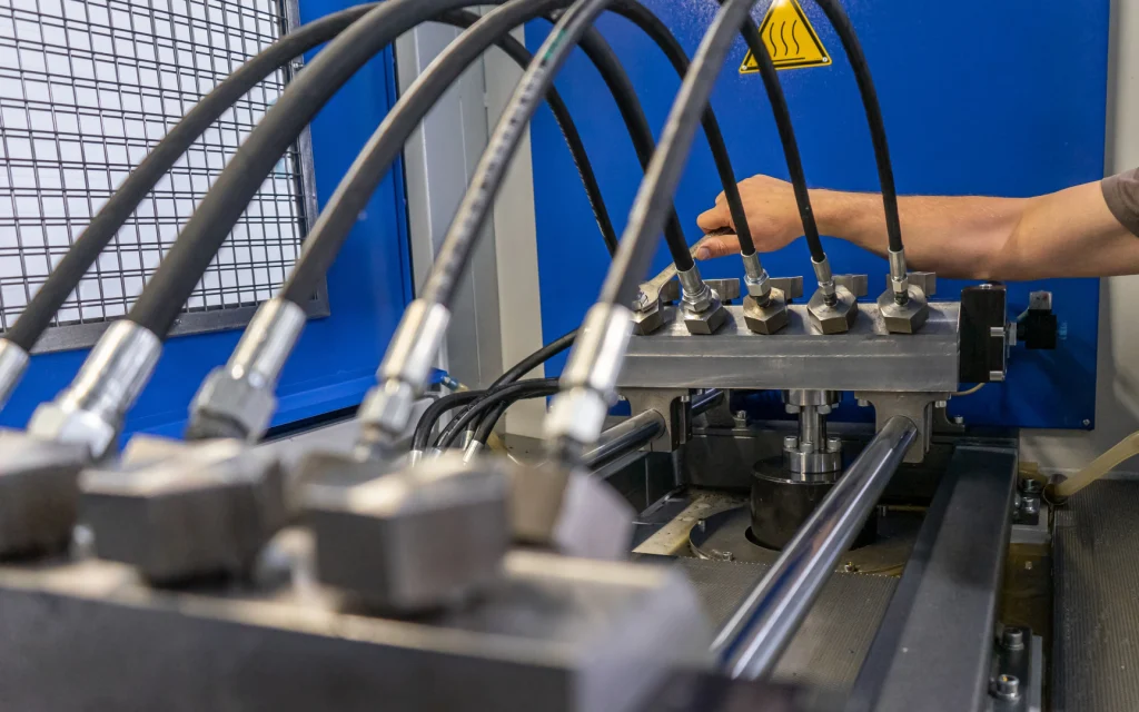 ✅ **Short Alt Text:** Person operating a complex machine with multiple hydraulic hoses in a factory, highlighting industrial hydraulic pressure testing work.