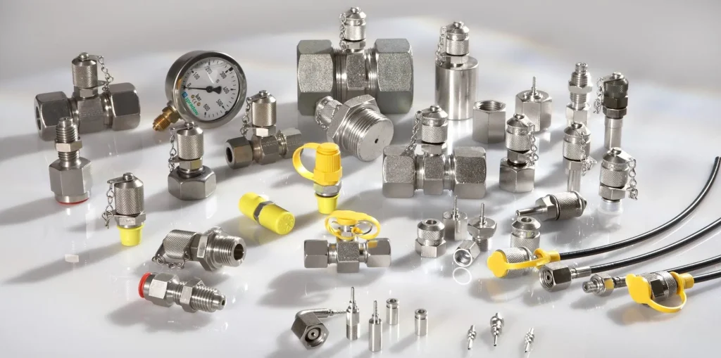 ✅ **Short Alt Text:** Metal fittings, valves, and a pressure gauge with yellow caps arranged on a white surface, used for hydraulic pressure testing.